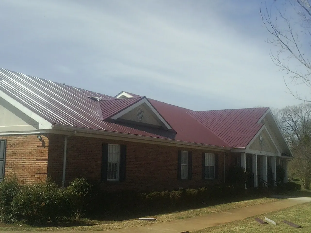 Red metal roof with gabled entries on a long brick building, from a Hail Damage Roof Repair job in Harford