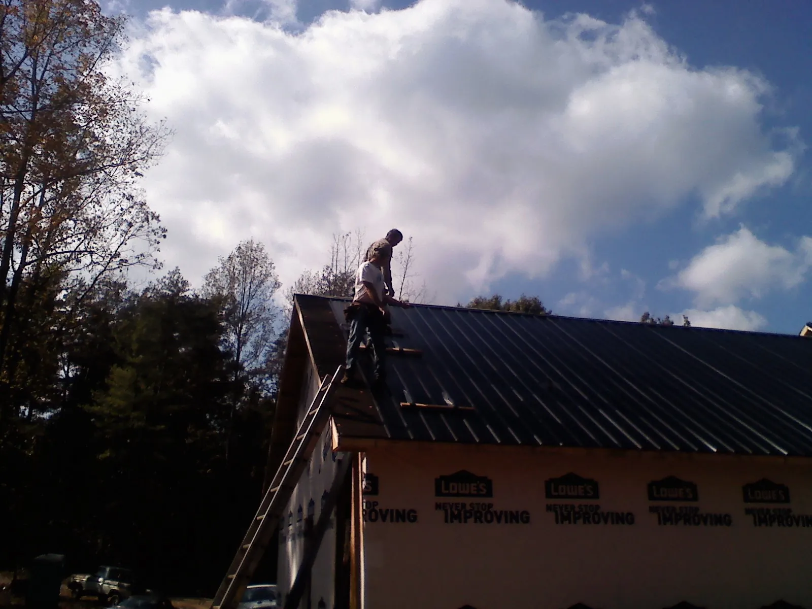 Roofer fastening dark metal panels high against a cloudy sky, from a Roof Inspection job in Harford