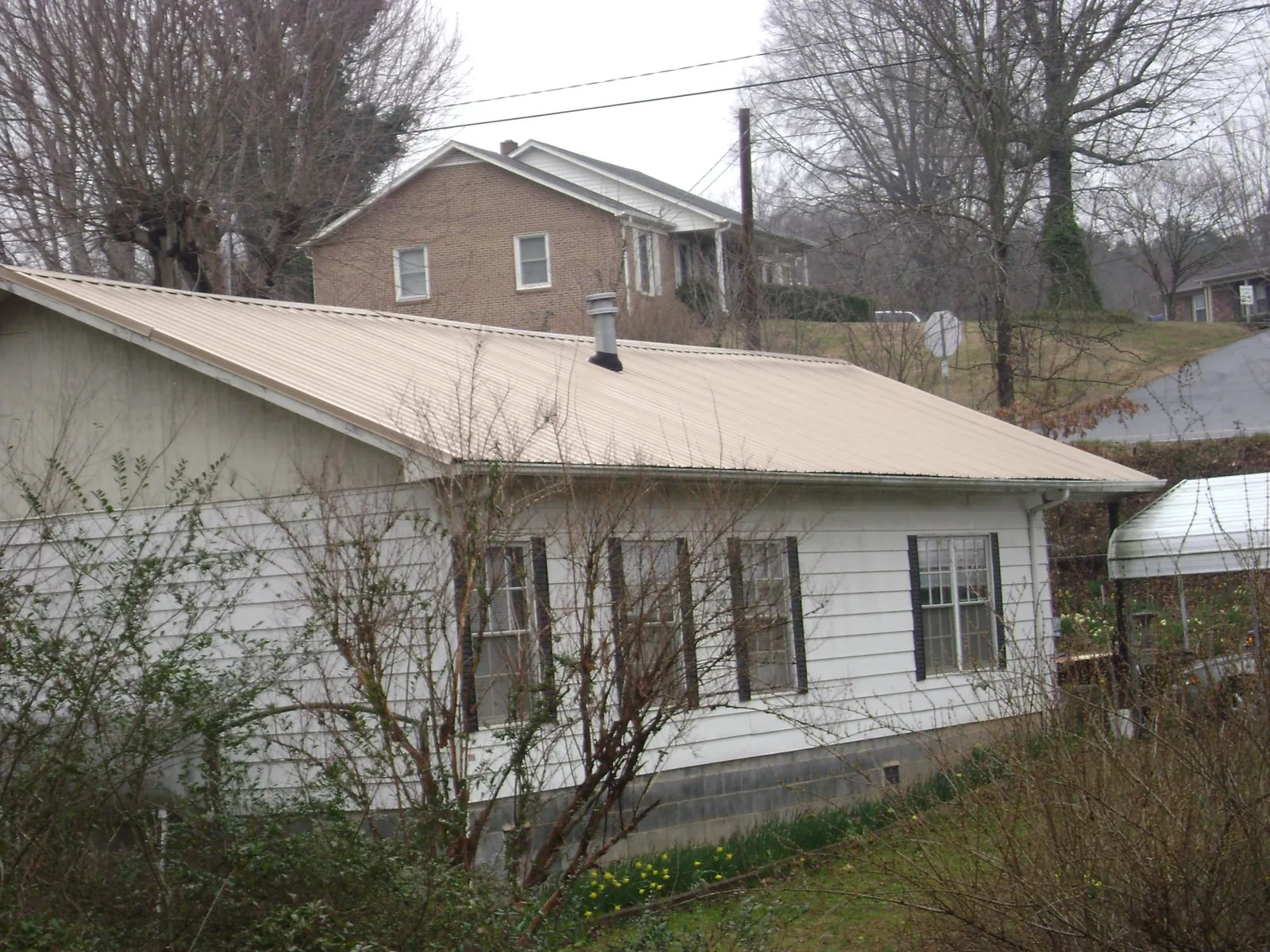 Tan metal roof on a white sided house set into a hillside — Commercial Roofing by Roofing Brothers in Harford